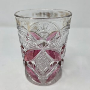 May include: A clear, vintage-style glass with a decorative pattern and pink accents. The glass has a thick base and a detailed, cut-glass design, perfect for serving beverages. The pink color is visible in the cut-glass design.