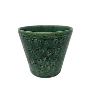 May include: A dark green ceramic planter with a textured, pitted surface. The planter has a slightly flared shape, wider at the top than the base. The interior is smooth, and the exterior has a rough, organic appearance.
