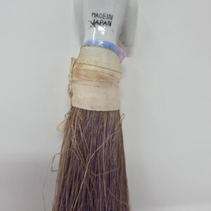 May include: A vintage doll with a porcelain head and a bundle of brown and purple fibres. The doll's head is white with pink accents and the text "MADE IN JAPAN" is visible.