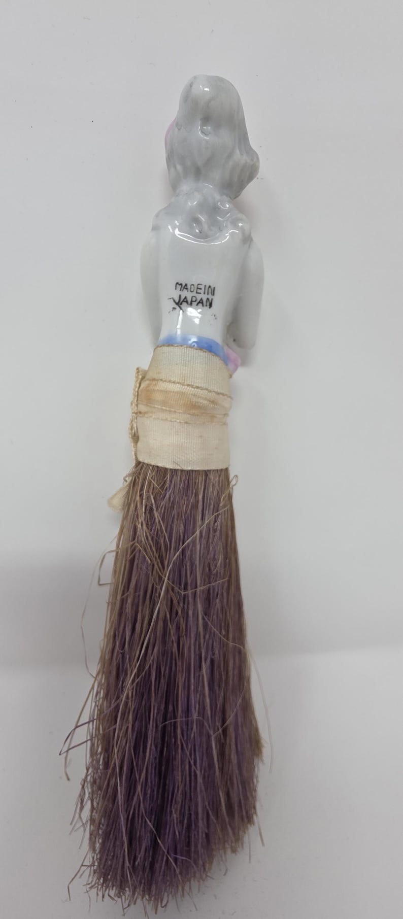 May include: A vintage doll with a porcelain head and a bundle of brown and purple fibres. The doll's head is white with pink accents and the text "MADE IN JAPAN" is visible.