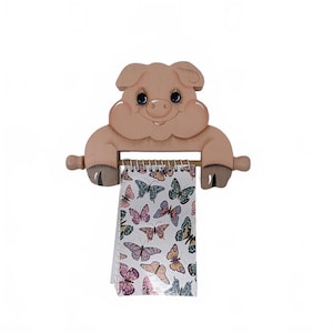 May include: A light pink wooden pig-shaped wall mount featuring a horizontal rod that holds a spiral-bound notepad. The notepad pages are decorated with a repeating pattern of colorful butterflies in shades of purple, blue, orange, and green.