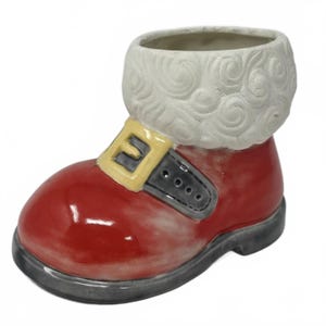 Peut inclure: Un pot de fleur en forme de botte de Père Noël en céramique rouge brillant, avec une bordure blanche bouclée sur le dessus. La botte présente une boucle jaune avec une sangle grise et une semelle grise. Décoration de vacances festive.