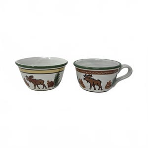 May include: Two ceramic bowls with a moose design. One bowl has a handle. The bowls are white with a green and yellow rim. The moose is brown, and there are brown and green accents.
