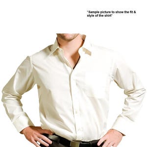 May include: A white long-sleeved dress shirt with a button-down collar and a single chest pocket. The shirt is tucked into black pants with a black belt.
