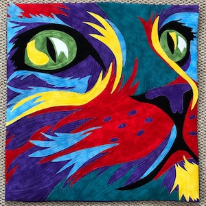 May include: A colourful abstract quilt depicting a cat's face. The quilt is made of various fabrics in shades of red, blue, yellow, green, and purple. The cat's eye is a vibrant green with a yellow pupil.