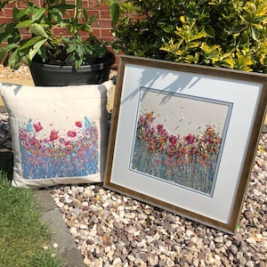 Pode incluir: Duas peças de bordado emolduradas que representam um campo de flores coloridas. A peça menor é uma almofada com fundo branco e a peça maior é uma obra de arte emoldurada com um passe-partout branco.