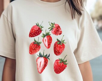 May include: A cream-colored t-shirt with a graphic print of red strawberries. The strawberries are arranged in a cluster on the front of the shirt.