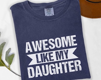May include: A navy blue t-shirt with white text that reads "Awesome Like My Daughter". The text has a distressed look.