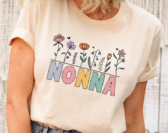 May include: A cream-colored t-shirt with a floral design and the word "NONNA" in colorful letters.