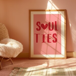 May include: A gold framed print with a pink background and the text "SOUL TIES" in red with a red heart in the middle of the word "SOUL".