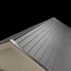 May include: A section of a gray metal roof with a corrugated design. The roof has a slight angle, with a dark background. The roof's edge is trimmed with a dark metal flashing.