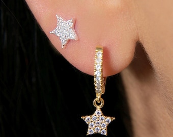 May include: A pair of gold star earrings. One earring is a small star stud, the other is a larger star dangling from a hoop.