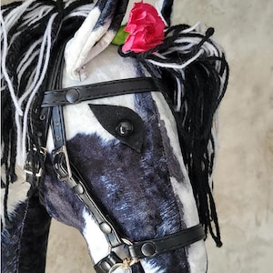 May include: A black and white plush horse head with a black leather bridle and a pink flower on its head.