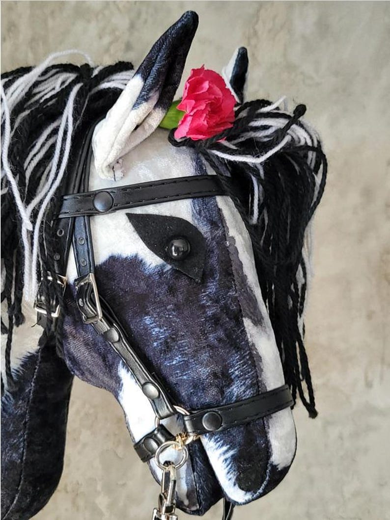 May include: A black and white plush horse head with a black leather bridle and a pink flower on its head.