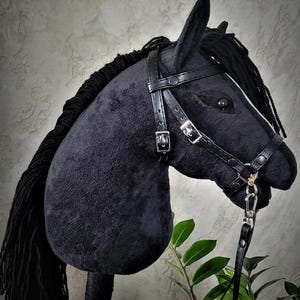May include: Black plush horse head with a black leather bridle and reins. The horse has a black mane and tail. The horse is on a wooden stick.