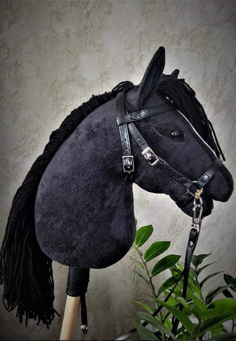 May include: Black plush horse head with a black leather bridle and reins. The horse has a black mane and tail. The horse is on a wooden stick.