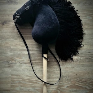 May include: A black plush rocking horse with a wooden stick handle and a black leather strap. The horse has a long black mane and tail.