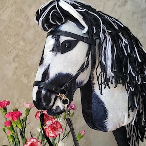 May include: A black and white plush horse head with a black leather bridle and reins. The horse has a long, black and white mane and tail.
