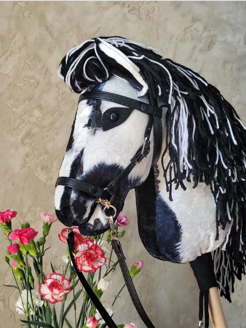 May include: A black and white plush horse head with a black leather bridle and reins. The horse has a long, black and white mane and tail.