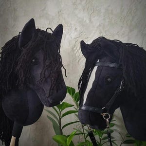 May include: Two black hobby horse heads with black yarn manes. One horse has a white stripe on its face and a black leather bridle.