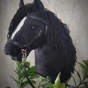 May include: Black horse head with a white stripe on its face, wearing a black leather bridle with a silver buckle. The horse head is made of plush fabric and has a long black mane.