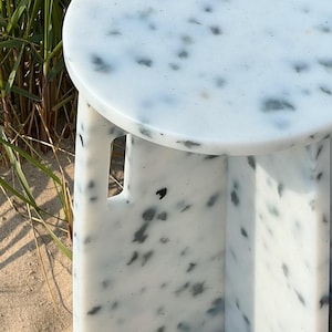 Peut inclure: Une table d'appoint ronde blanche et noire mouchet&eacute;e avec un design unique. La table a un dessus arrondi et un pi&eacute;tement &agrave; trois pieds.