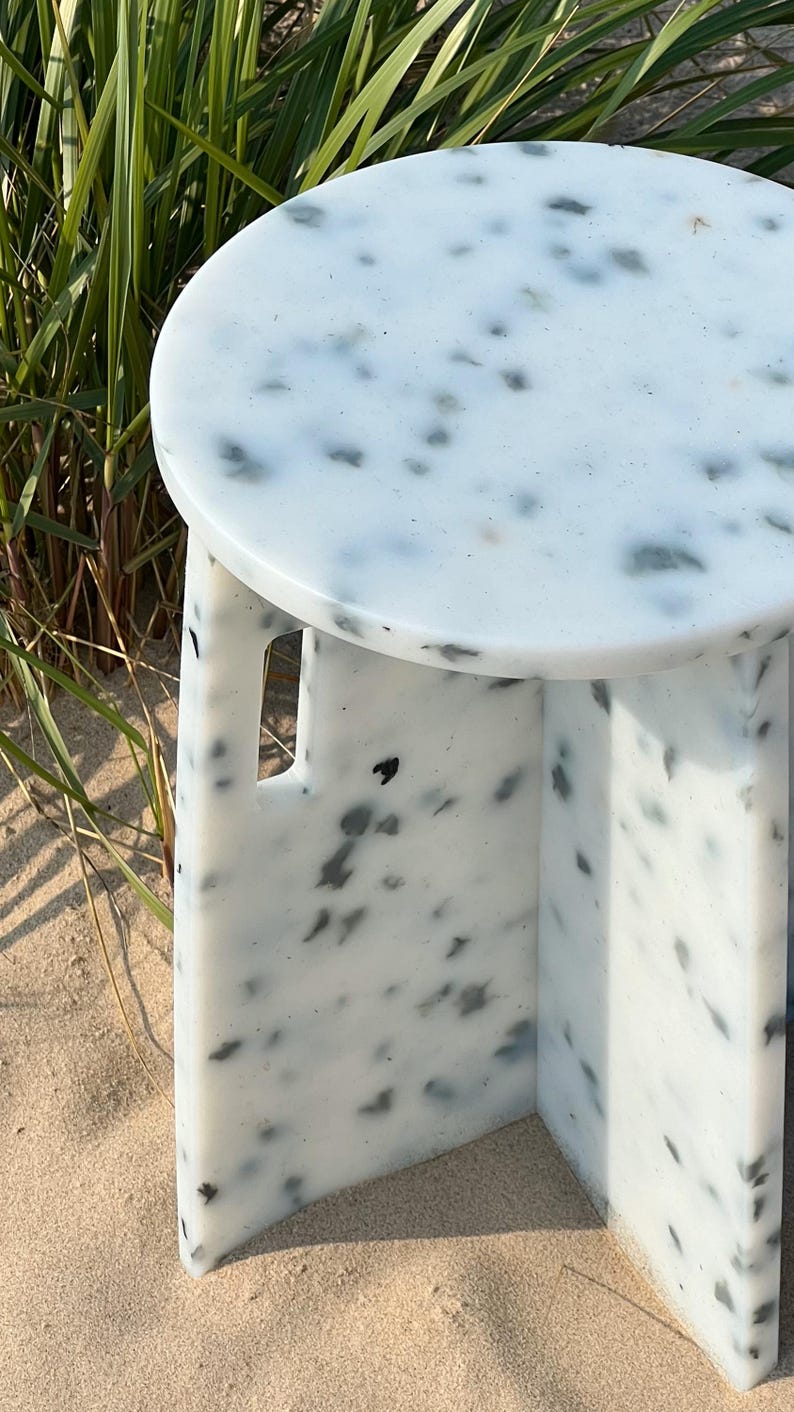 Peut inclure: Une table d'appoint ronde blanche et noire mouchet&eacute;e avec un design unique. La table a un dessus arrondi et un pi&eacute;tement &agrave; trois pieds.