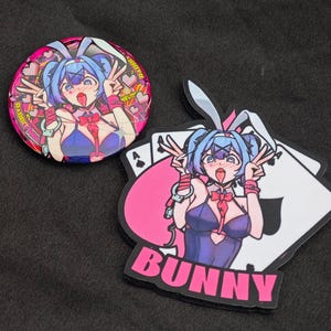 以下が含まれることがあります： ピンクとブルーのアニメ風のキャラクターで、ウサギの耳とピンクのリボンをしています。キャラクターは、ハート型のカットアウトのある青と紫の衣装を着ています。キャラクターはピースサインで2本の指を立てています。背景は、黒いスペードのシンボルが付いたピンクと白のトランプです。キャラクターの下にピンクの文字で「BUNNY」と書かれています。