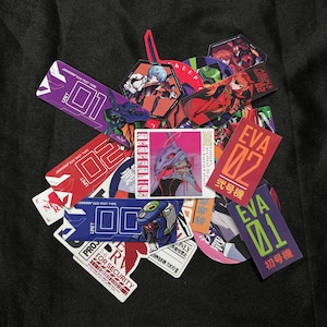May include: A collection of colorful stickers featuring anime characters and Japanese text. The stickers have various shapes and sizes, with images of robots and characters. Some stickers have the text "EVA 01" and "EVA 02".