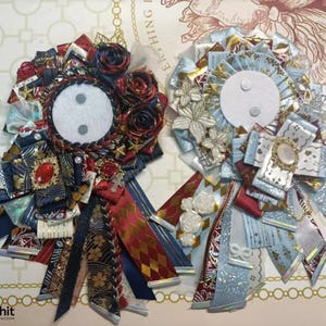 May include: Two decorative rosettes with intricate ribbon designs. One features red, navy, and gold ribbons with a central white circle and a red jewel. The other has light blue, white, and gold ribbons with a central white circle and a decorative brooch.