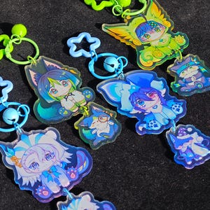 May include: Four colorful keychains with cartoon characters. Each keychain features a character with blue and green hair, wearing a blue and green outfit. The characters are holding a small animal in their hands. The keychains are made of clear acrylic and have a star-shaped charm.