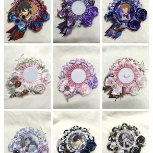 May include: Nine decorative rosette badges with various designs. Each badge features a central circular area, surrounded by ribbons, rosettes, and embellishments. Some include character illustrations, while others have blank centers. Colors include blue, purple, pink, and white.