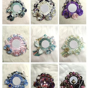 May include: Nine decorative rosettes in various colors, each featuring a central white circle. The rosettes are adorned with ribbons, bows, and fabric flowers in shades of blue, purple, pink, and mixed patterns. Some include embellishments.