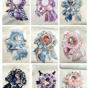 May include: A collection of nine decorative ribbon badges in various colors, including blue, purple, and pink. Each badge features a central image, surrounded by fabric flowers, ribbons, and decorative elements. The badges have a layered design.