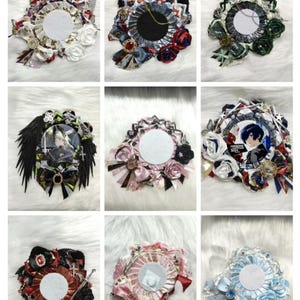 May include: A collection of decorative badges with a central circular space, surrounded by ribbons, bows, and embellishments. Some badges feature cat ears, feathers, or floral accents. Colors include red, black, white, and blue.