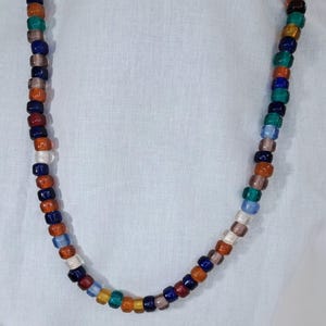 May include: A long necklace made of colorful glass beads. The beads are in shades of blue, green, orange, brown, and white.