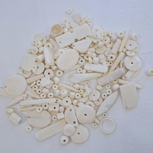 May include: A large collection of white bone beads and pendants. The beads are of various shapes and sizes, including round, oval, and rectangular. Some of the beads have intricate carvings.