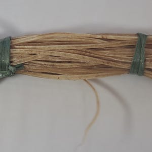 May include: A roll of light brown leather cord tied with green string. The cord is about 1/4 inch wide and is suitable for leather crafting projects.