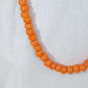 May include: A long orange necklace made of round beads. The beads are all the same size and shape, and they are strung together on a thin cord.