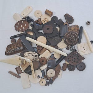May include: A collection of brown and white bone beads and pendants. The beads are of various shapes and sizes, including round, square, and rectangular. Some of the beads have intricate carvings.
