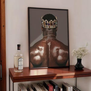 Pode incluir: Impress&atilde;o de arte emoldurada com uma figura musculosa usando uma coroa de joias e uma corrente de ouro. A obra de arte &eacute; exibida em uma prateleira de madeira escura, junto com uma garrafa de licor e um pequeno vaso de flores brancas. Fundo cinza escuro.