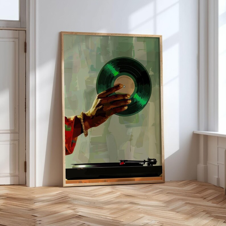 May include: A framed art print featuring a hand holding a green vinyl record. The artwork has a vintage aesthetic with a turntable at the bottom. The hand is adorned with a gold bracelet and ring, set against a muted green background.