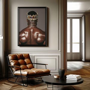 Pode incluir: Uma obra de arte emoldurada retrata uma pessoa de costas usando uma coroa de joias e uma corrente de ouro. A obra de arte est&aacute; pendurada acima de uma poltrona de couro marrom com uma estrutura de metal preta. Uma mesa de centro redonda preta e itens decorativos completam a cena.