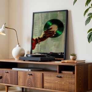 May include: A wooden media console with a framed art print of a hand holding a green vinyl record. A black turntable sits on top. A white lamp and a small plant are also on the console.