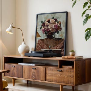 Puede incluir: Un mueble de medios de madera de estilo moderno de mediados de siglo con tres cajones y un estante. Un tocadiscos se encuentra en la parte superior del mueble, y una l&aacute;mpara de cer&aacute;mica blanca con una base dorada est&aacute; a la izquierda. Una impresi&oacute;n enmarcada de una mujer con flores cubriendo su rostro cuelga en la pared detr&aacute;s del mueble.