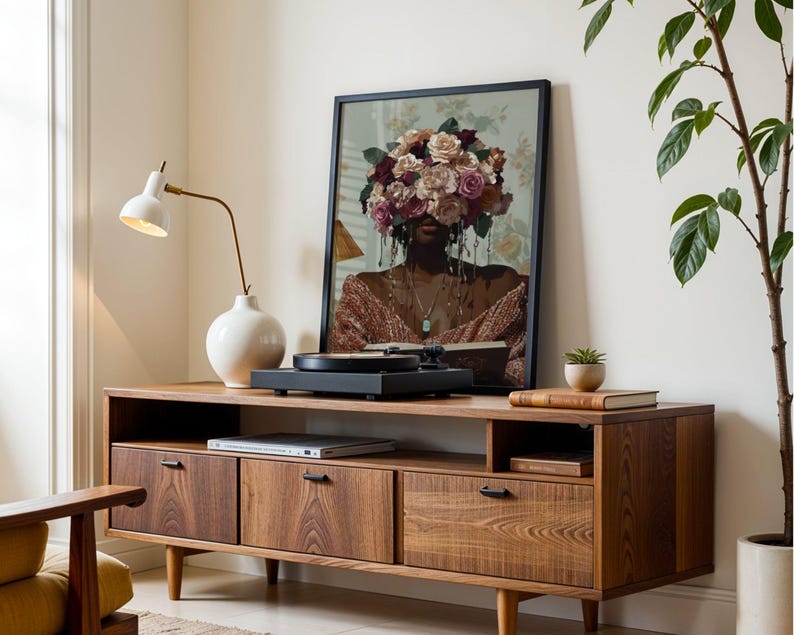 Puede incluir: Un mueble de medios de madera de estilo moderno de mediados de siglo con tres cajones y un estante. Un tocadiscos se encuentra en la parte superior del mueble, y una l&aacute;mpara de cer&aacute;mica blanca con una base dorada est&aacute; a la izquierda. Una impresi&oacute;n enmarcada de una mujer con flores cubriendo su rostro cuelga en la pared detr&aacute;s del mueble.