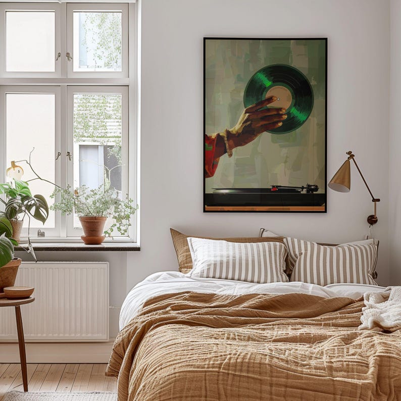 May include: A framed art print depicts a hand holding a green vinyl record above a turntable. The artwork has a vintage aesthetic, with a neutral background and a black frame. The bedroom setting includes a bed with brown bedding and striped pillows.