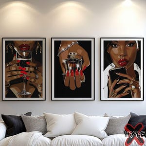 May include: Three framed art prints featuring a woman with red lipstick and nails. The prints are set against a white wall above a white couch. The woman in the left print is holding a glass of wine, the woman in the center print is holding a bottle of perfume, and the woman in the right print is holding a smartphone.