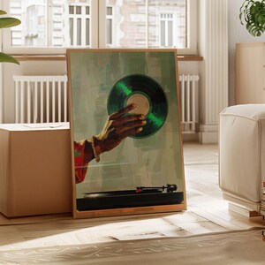 May include: A framed art print featuring a hand holding a green vinyl record. The artwork has a vintage aesthetic, with a turntable in the foreground. The hand has gold painted nails and is wearing a bracelet. The background is a muted green.