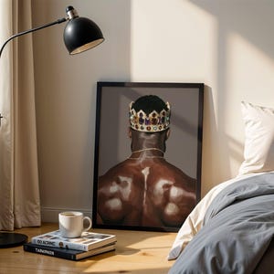 Pode incluir: Uma impress&atilde;o de arte emoldurada retrata uma pessoa usando uma coroa de joias, vista por tr&aacute;s. A obra de arte &eacute; exibida no ch&atilde;o ao lado de uma cama com roupa de cama cinza. Uma lumin&aacute;ria de ch&atilde;o preta e livros com uma x&iacute;cara de caf&eacute; tamb&eacute;m s&atilde;o vis&iacute;veis.